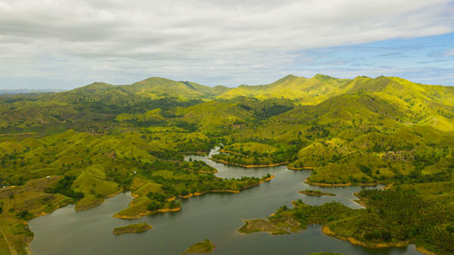 Lake among mountains and hills with rainforest and green grass under a blue sky with clouds