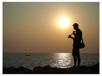 Silhouette man standing by sea against sky during sunset