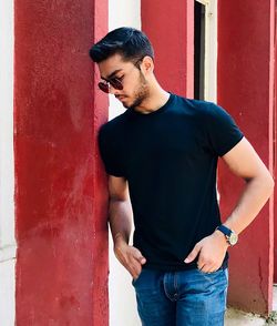 Young man looking away while standing against wall