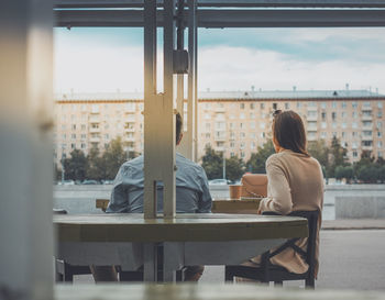 Rear view of woman sitting on table against window in city