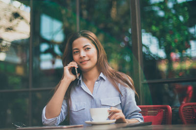 Young woman using phone while sitting on table at sidewalk cafe