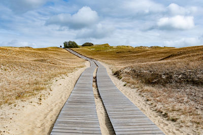 Boardwalk leading towards field against sky