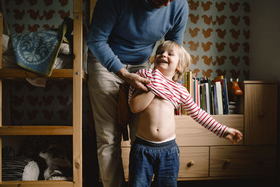 Father dressing cheerful daughter at home