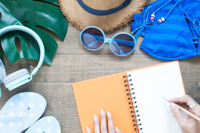 Cropped hand of woman writing on book by personal accessories