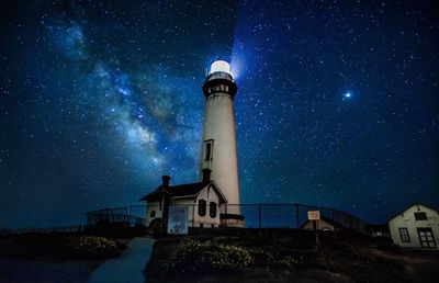 Low angle view of lighthouse against buildings at night