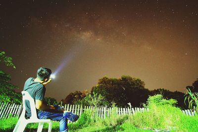 Man sitting on chair against sky at night