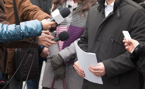 Cropped image of journalist holding microphones in front of people