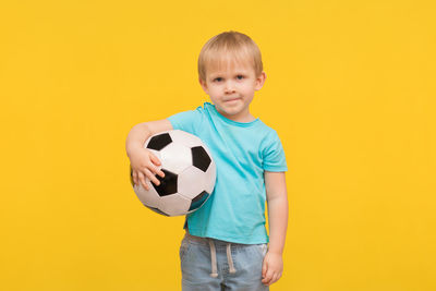 Boy playing soccer ball against yellow background