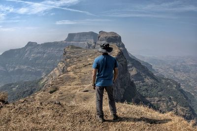 Rear view of man standing on mountain against sky