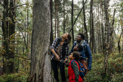 Mother looking up while standing near tree with family during vacation in forest