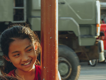 Close-up of smiling girl looking away by pole