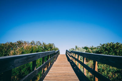 Footbridge amidst trees against clear blue sky