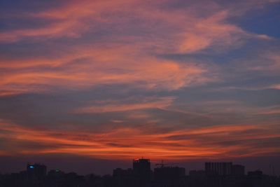 Silhouette cityscape against dramatic sky at sunset