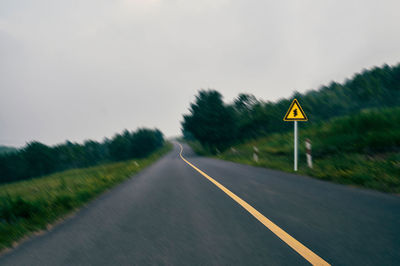 Road sign on field against sky
