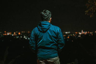 Rear view of man looking at illuminated city at night