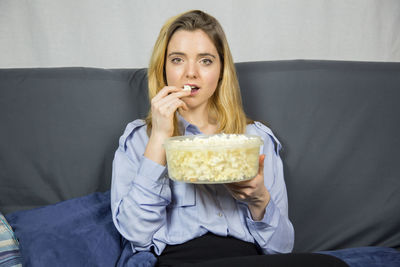 Portrait of young woman having popcorn while sitting on sofa at home