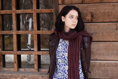 Young woman looking away while leaning on wooden wall