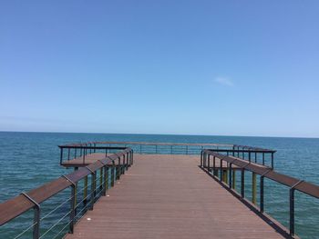 Pier over sea against clear blue sky