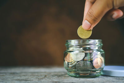 Cropped hand putting coin in glass container on wooden table