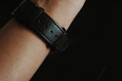 Cropped hand wearing wristwatch against black background