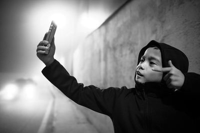 Boy gesturing while taking selfie on sidewalk at morning