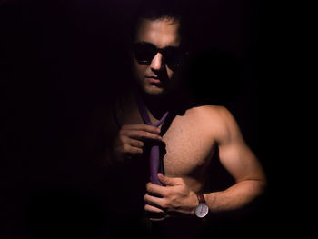 Portrait of shirtless young man holding cigarette against black background