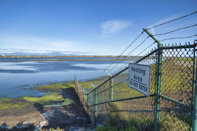 View of information sign by fence against sky