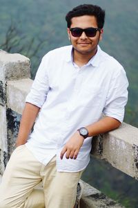 Portrait of young man wearing sunglasses standing on retaining wall