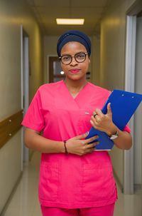 Portrait of a young nurse holding a folder against hospital corridor 