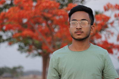 Portrait of young man looking away against trees