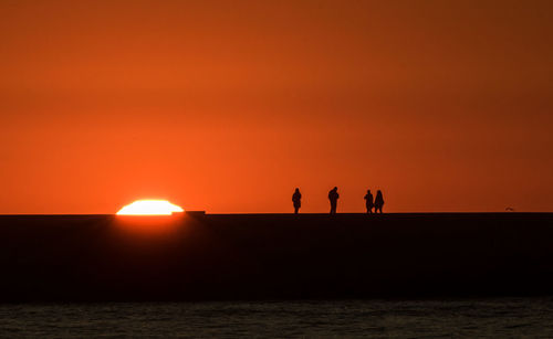 Silhouette people by sea against orange sky