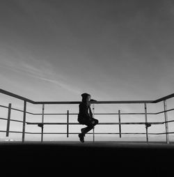 Girl sitting by railing at promenade against sky