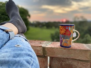 Low section of man with drink sitting against sky