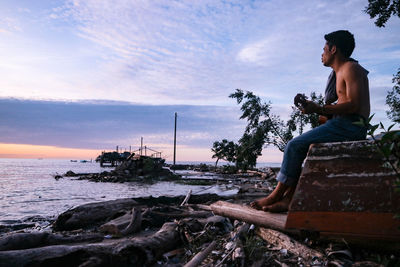 Man sitting on rock at beach against sky