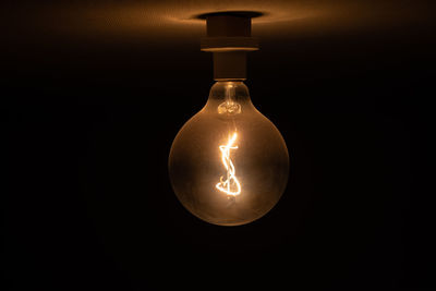 Close-up of illuminated light bulb against black background