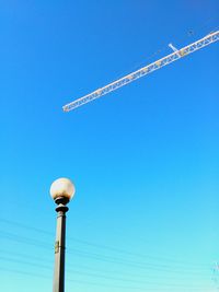 Low angle view of street light and cranes against clear blue sky on sunny day