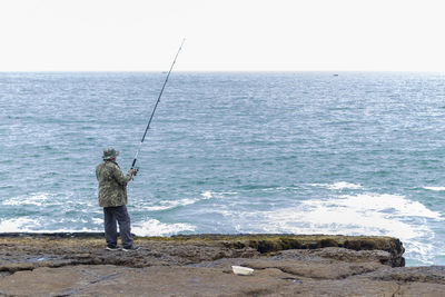 Rear view of man fishing on sea against sky