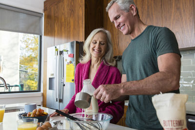 Man preparing food while standing by smiling woman in kitchen at home