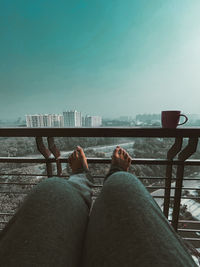 Low section of man relaxing on railing by sea against sky