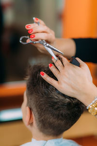 Boy getting a new haircut. female hairstylist cutting his black hair with scissors in hair salon