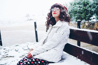 Woman sitting on snow covered bench during winter