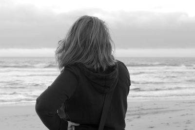 Rear view of woman standing at beach against cloudy sky