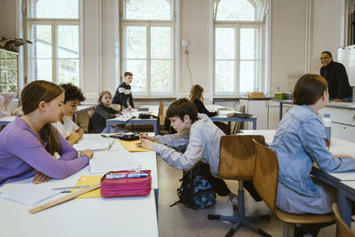 Schoolboy assisting friends sitting on desk in classroom