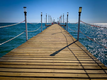 Pier over sea against clear blue sky