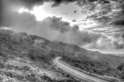 Road leading towards mountains against cloudy sky