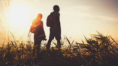 Man and woman standing on field against sky during sunset