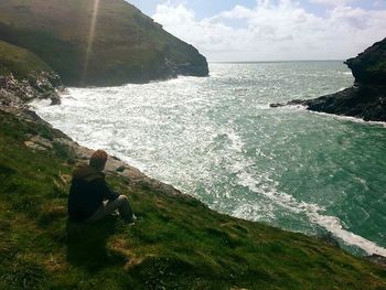 Rear view of man sitting on cliff by sea