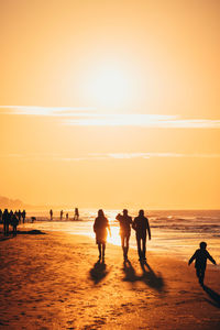 Silhouette people on beach against sky during sunset