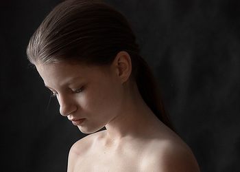 Close-up of shirtless young woman against black background