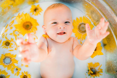 Portrait of cute baby boy with yellow flower in bathtub